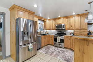 Kitchen featuring stainless steel appliances, hanging light fixtures, light tile patterned flooring, light countertops, and a kitchen breakfast bar
