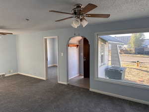 Spare room featuring ceiling fan, a textured ceiling, arched walkways, and dark colored carpet