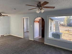 Empty room featuring a ceiling fan, arched walkways, a textured ceiling, and dark colored carpet