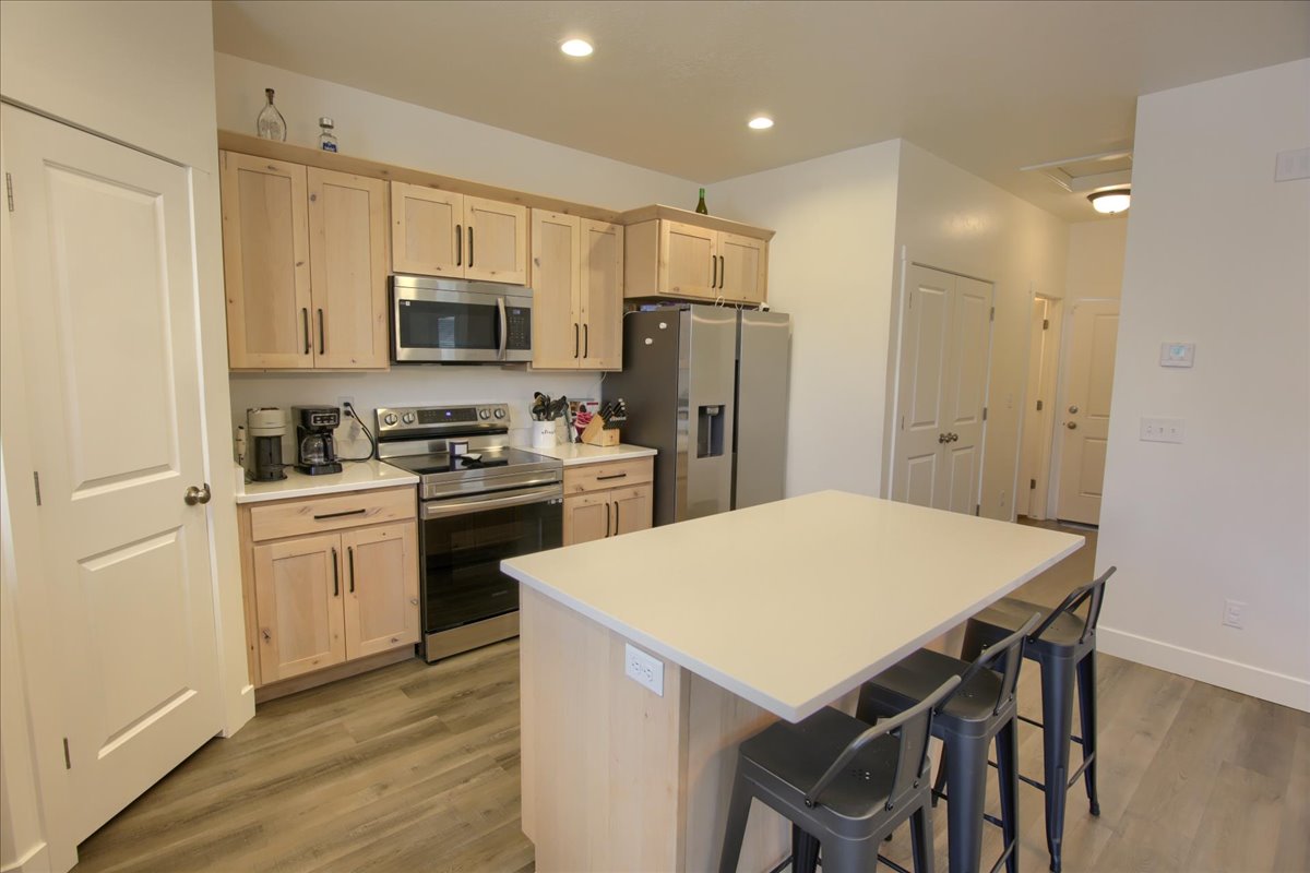 Kitchen with stainless steel appliances, a kitchen island, light wood finish cabinetry, light countertops, and a kitchen breakfast bar