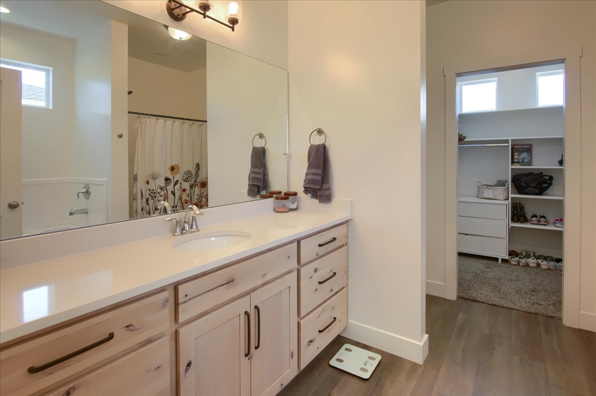 Full bath featuring a spacious closet, vanity, a shower with curtain, and dark wood-style floors