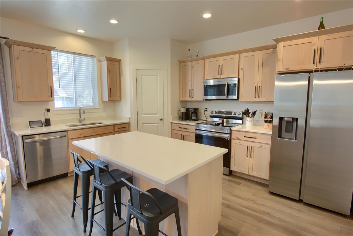 Kitchen featuring stainless steel appliances, light countertops, light wood finish cabinetry, light wood finished floors, and a center island