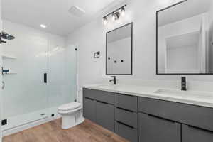 Bathroom with double vanity, a stall shower, light wood finished floors, and recessed lighting