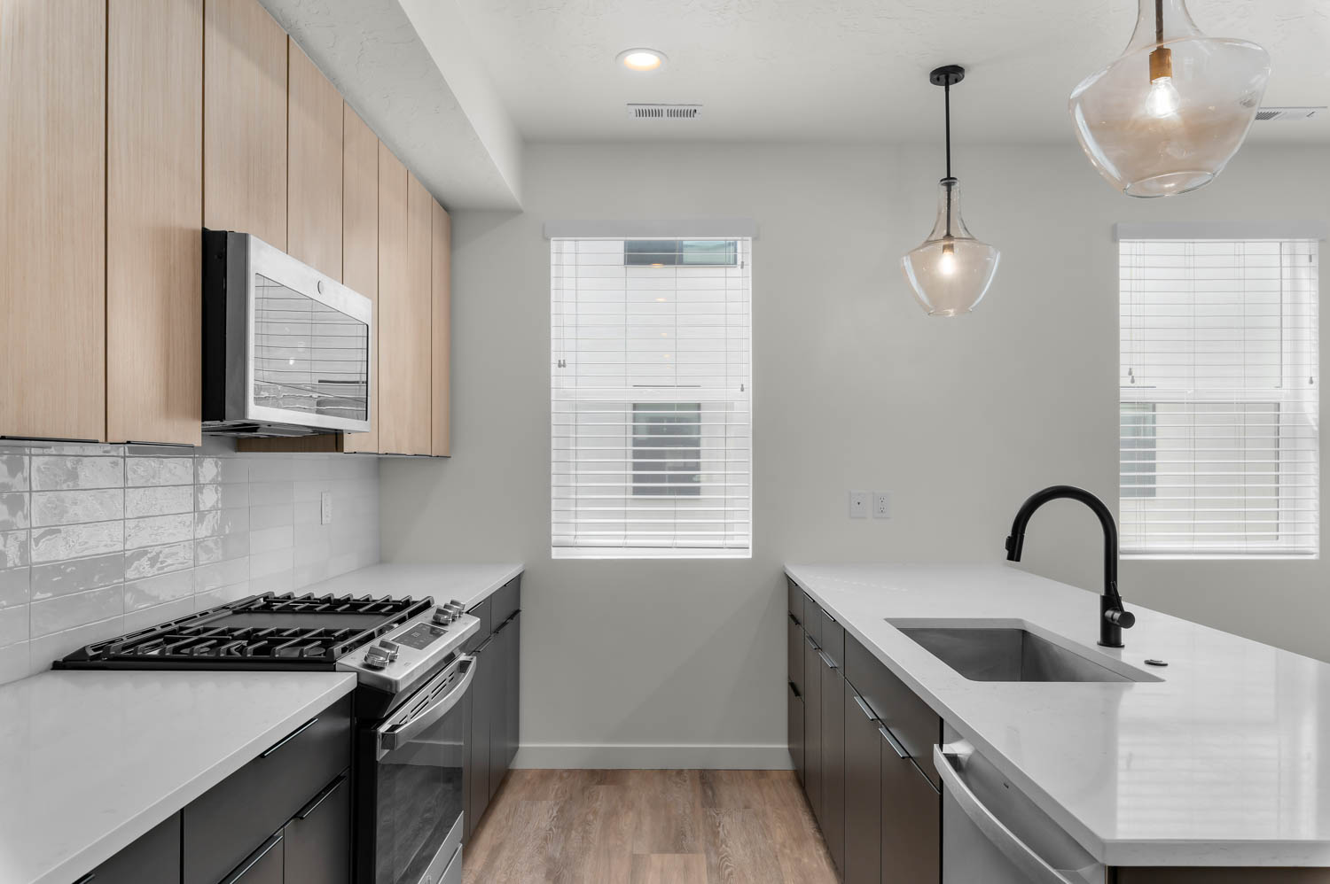Kitchen with a peninsula, stainless steel appliances, light stone countertops, decorative light fixtures, and light wood-style flooring