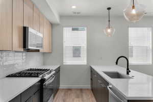 Kitchen with a peninsula, stainless steel appliances, light stone countertops, decorative light fixtures, and light wood-style flooring