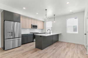 Kitchen with stainless steel appliances, a peninsula, decorative light fixtures, tasteful backsplash, and light wood-style floors