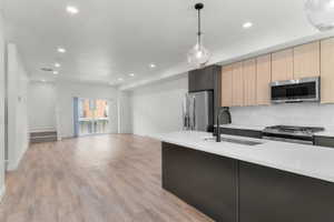 Kitchen featuring modern cabinets, stainless steel appliances, light stone countertops, light wood finish cabinetry, and open floor plan