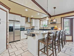Kitchen featuring a breakfast bar area, white cabinetry, dark stone countertops, stainless steel appliances, and crown molding
