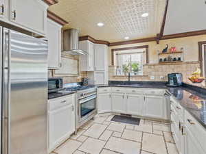 Kitchen featuring stainless steel appliances, white cabinetry, stone tile floors, dark stone countertops, and an ornate ceiling