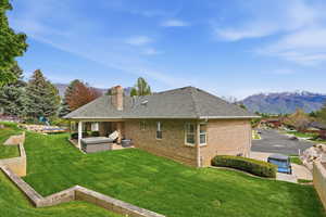 Back of house featuring a mountain view, a hot tub, a patio, brick siding, and a lawn