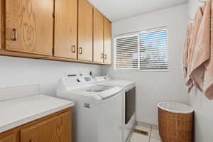 Laundry room featuring washing machine and clothes dryer, light tile patterned floors, and cabinet space