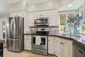 Kitchen with stainless steel appliances, decorative backsplash, white cabinetry, tile counters, and recessed lighting