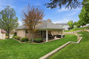 Back of property with a patio area, a hot tub, brick siding, and a lawn