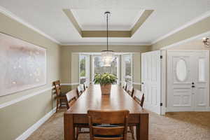 Dining space with hanging lights, a raised ceiling, carpet, a textured ceiling, and crown molding