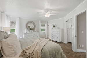 Bedroom with a textured ceiling, crown molding, dark carpet, a ceiling fan, and a closet