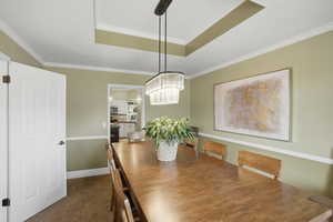 Dining room with a raised ceiling, ornamental molding, dark colored carpet, and hanging lights