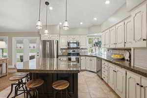 Kitchen featuring a kitchen breakfast bar, tasteful backsplash, stainless steel appliances, a kitchen island, and decorative light fixtures