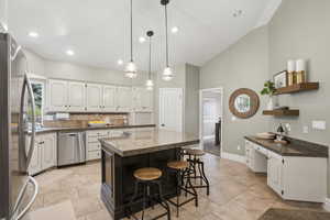 Kitchen featuring a breakfast bar, white cabinetry, stainless steel appliances, a kitchen island, and open shelves