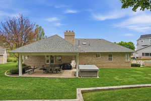 Back of property featuring roof with shingles, a lawn, a patio area, brick siding, and a chimney