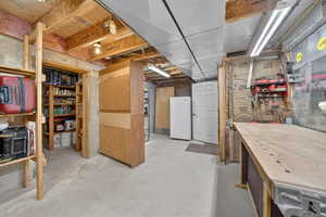 Unfinished below grade area with freestanding refrigerator and a workshop area
