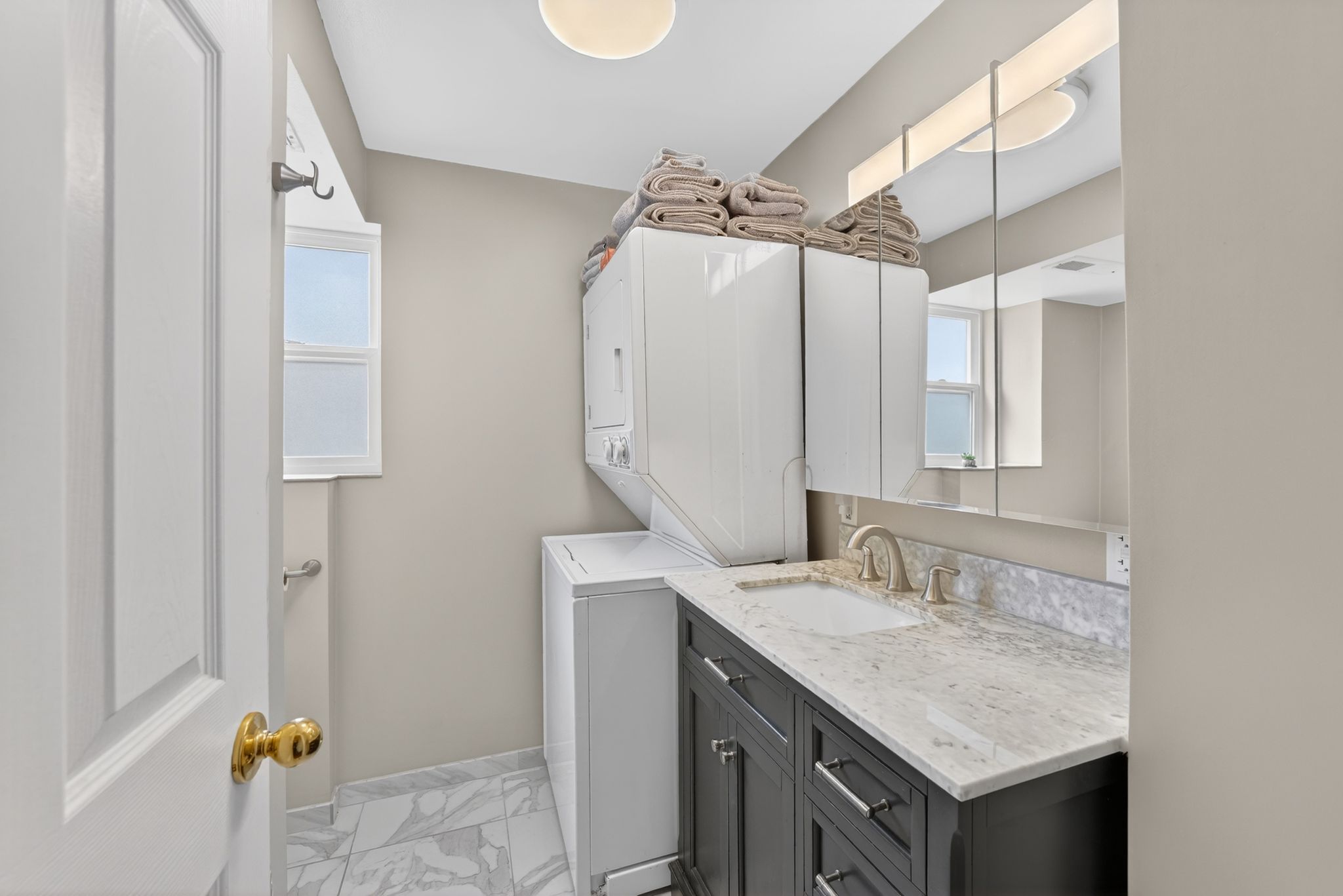 Bathroom with vanity, light marble finish flooring, stacked washer and clothes dryer, and plenty of natural light