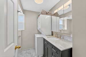 Bathroom with vanity, light marble finish flooring, stacked washer and clothes dryer, and plenty of natural light