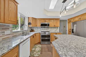 Kitchen featuring stainless steel appliances, light stone counters, decorative light fixtures, a raised ceiling, and decorative backsplash