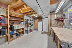 Unfinished basement with freestanding refrigerator and a workshop area
