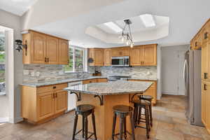 Kitchen featuring a breakfast bar area, a tray ceiling, light stone countertops, a skylight, and stainless steel appliances