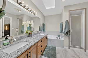 Full bathroom featuring a stall shower, double vanity, a bath, and a skylight