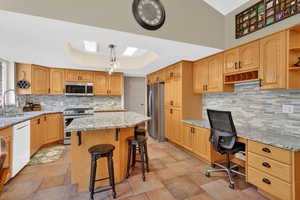 Kitchen featuring a tray ceiling, light stone counters, stainless steel appliances, a breakfast bar, and an office area