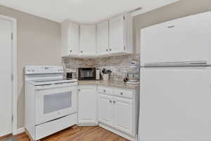 Kitchen featuring white appliances, light wood-type flooring, white cabinetry, and decorative backsplash