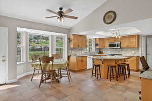 Dining area featuring a ceiling fan, lofted ceiling, suspended lighting, a tray ceiling, and light stone finish flooring