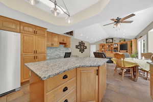 Kitchen with freestanding refrigerator, a kitchen island, open floor plan, light stone counters, and ceiling fan