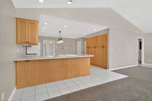 Kitchen with light tile patterned floors, a peninsula, light countertops, decorative light fixtures, and lofted ceiling
