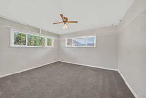 Empty room featuring dark carpet, plenty of natural light, and ceiling fan