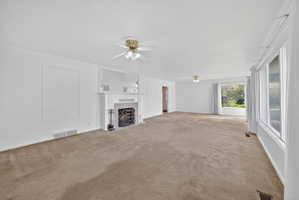 Unfurnished living room featuring a ceiling fan, a tiled fireplace, and carpet floors