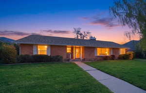 Ranch-style house with a front yard, brick siding, a chimney, and a shingled roof