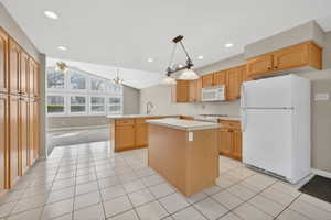 Kitchen featuring white appliances, lofted ceiling, light countertops, a peninsula, and decorative light fixtures