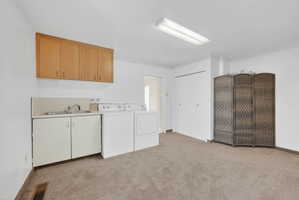 Laundry area featuring light colored carpet, cabinet space, and washing machine and dryer