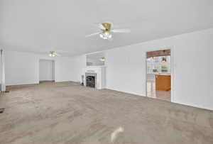 Unfurnished living room featuring light colored carpet, a fireplace with flush hearth, and ceiling fan