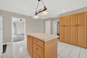 Kitchen with light wood finish cabinets, light countertops, a kitchen island, hanging light fixtures, and light carpet