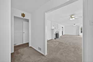 Unfurnished living room featuring a fireplace, light colored carpet, and ceiling fan