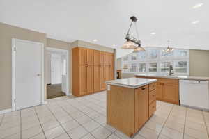 Kitchen with white dishwasher, decorative light fixtures, light countertops, light tile patterned floors, and a kitchen island