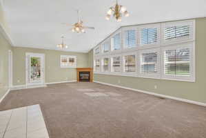 Unfurnished living room featuring hanging lights, a glass covered fireplace, light colored carpet, a ceiling fan, and a high ceiling