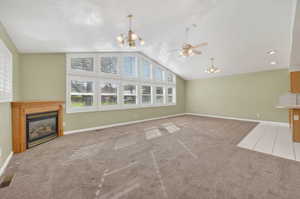 Unfurnished living room featuring hanging lights, a glass covered fireplace, light carpet, a ceiling fan, and a high ceiling