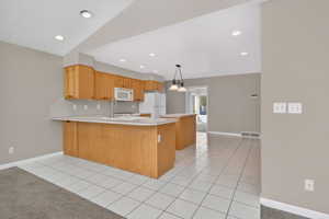 Kitchen featuring light tile patterned floors, light countertops, a peninsula, white appliances, and lofted ceiling