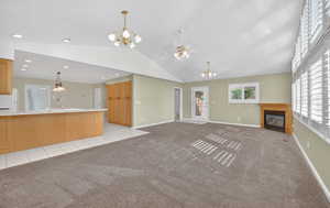 Unfurnished living room with hanging lights, light colored carpet, a glass covered fireplace, lofted ceiling, and light tile patterned floors