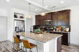 Kitchen with light stone counters, a breakfast bar area, light wood finished floors, and stainless steel appliances
