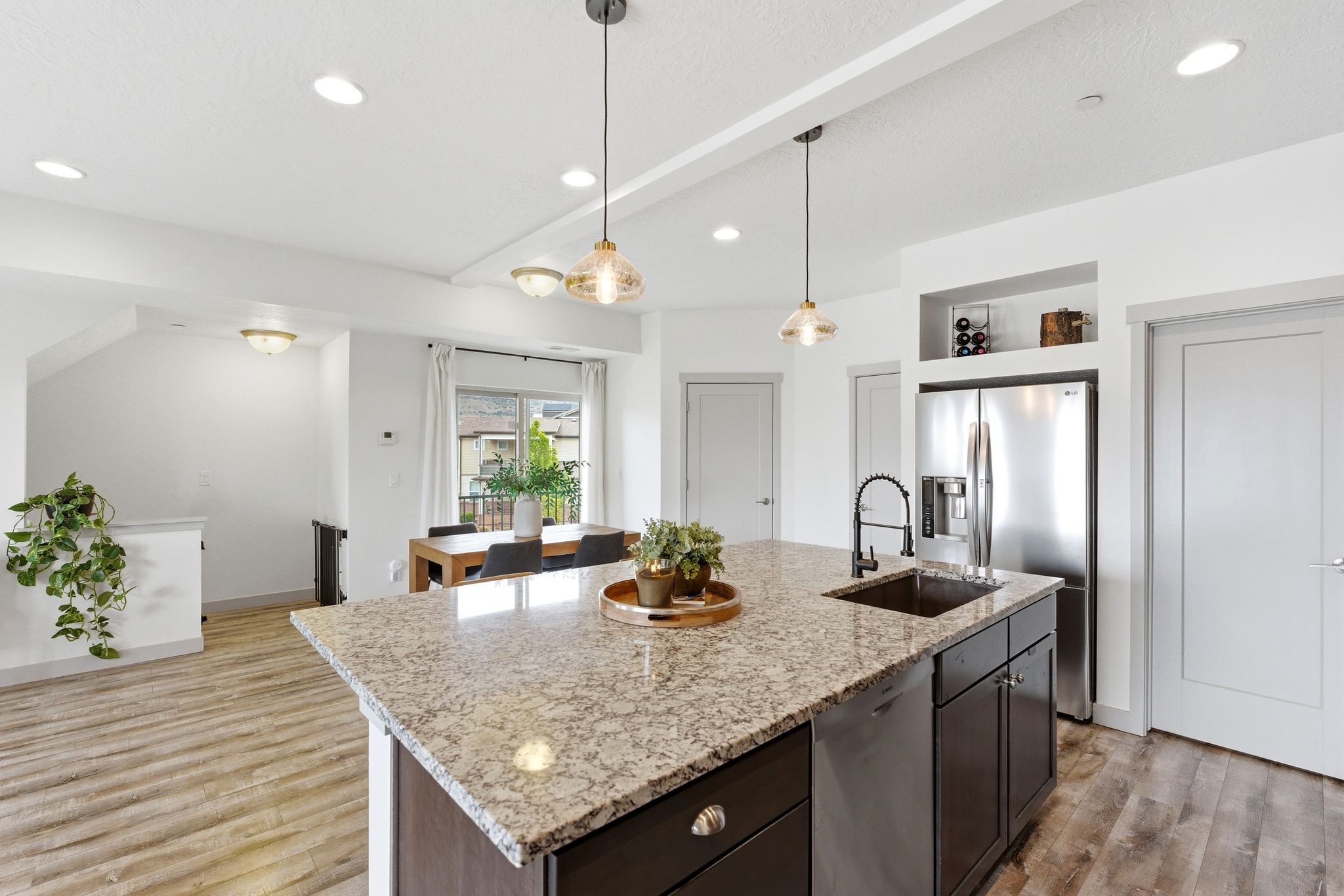 Kitchen with a kitchen island with sink, light stone countertops, stainless steel appliances, pendant lighting, and light wood-style floors